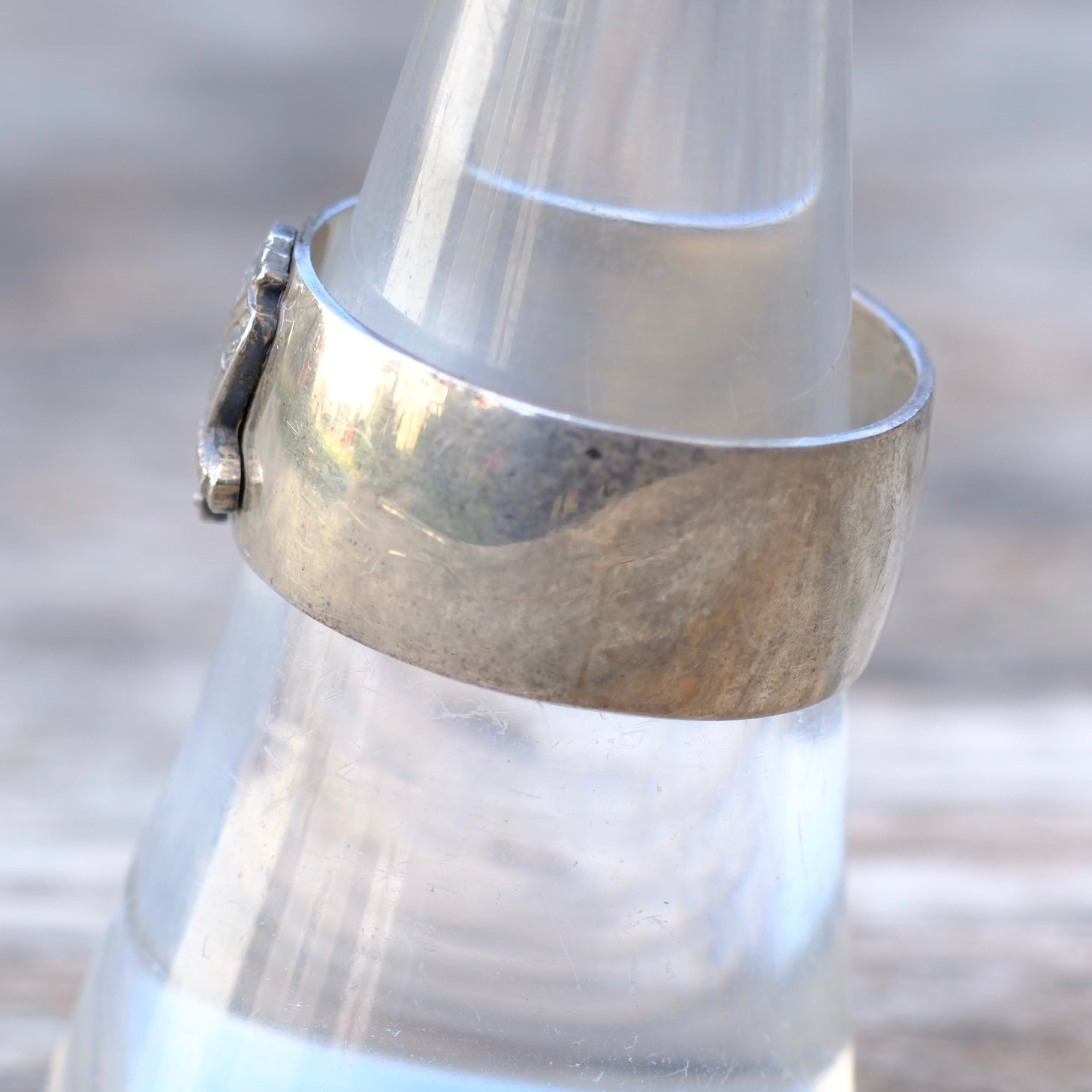 Close-up of a silver bracelet on a glass bottle with a blurred natural background