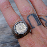 Close-up of a hand wearing a coin ring with a blurred background