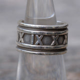 Silver ring with Roman numeral design on a reflective surface