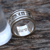 Silver ring with Roman numeral design on a wooden surface, featuring Tiffany & Co. branding.
