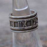 Silver ring with Roman numeral design on a metallic surface