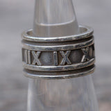 Silver ring with Roman numeral design on a blurred background