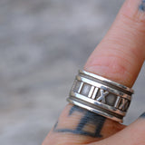 Silver ring with Roman numeral design on a finger against a blurred background