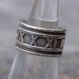 Silver ring with Roman numeral design on a metallic surface