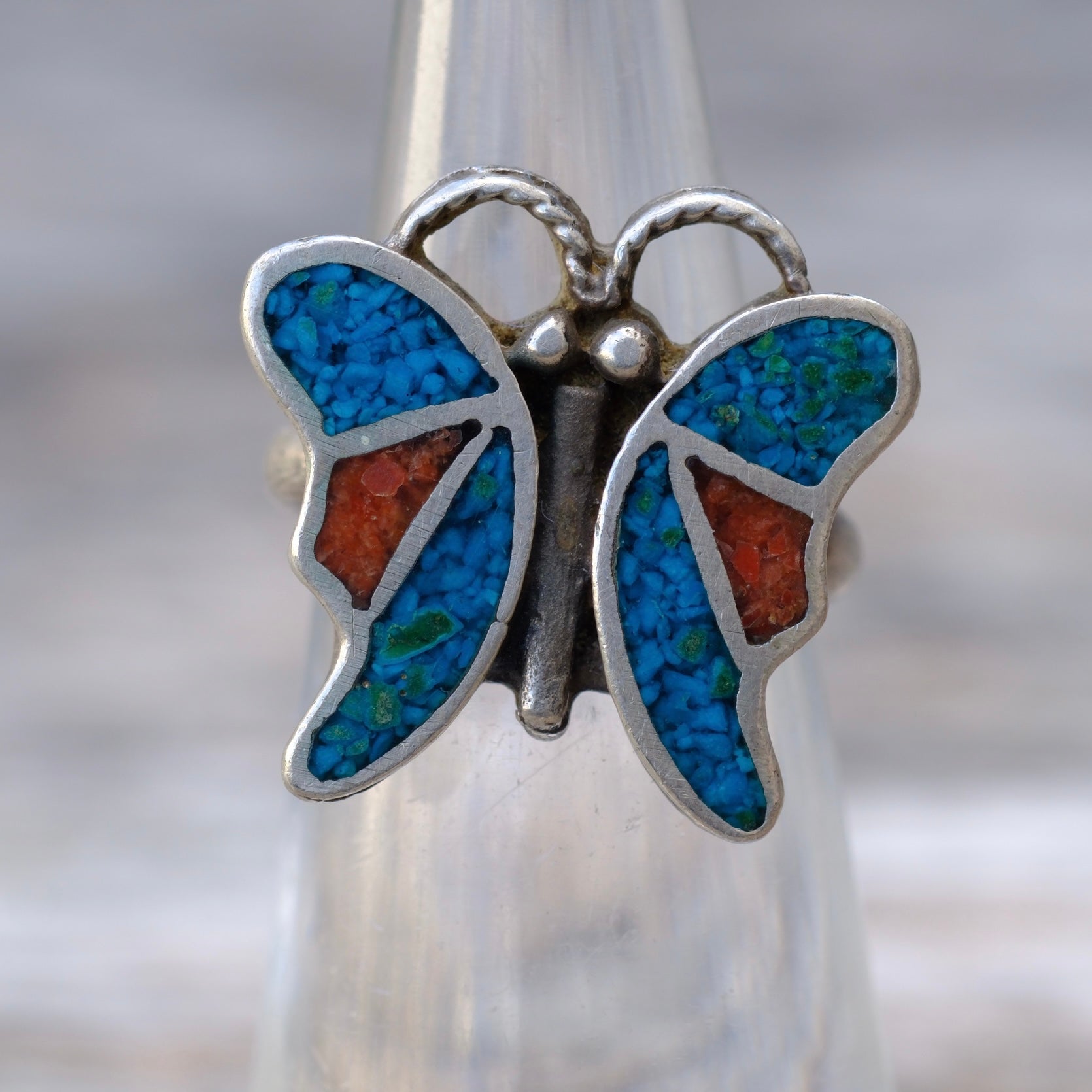 Butterfly-shaped pendant with blue and orange inlay on a blurred background
