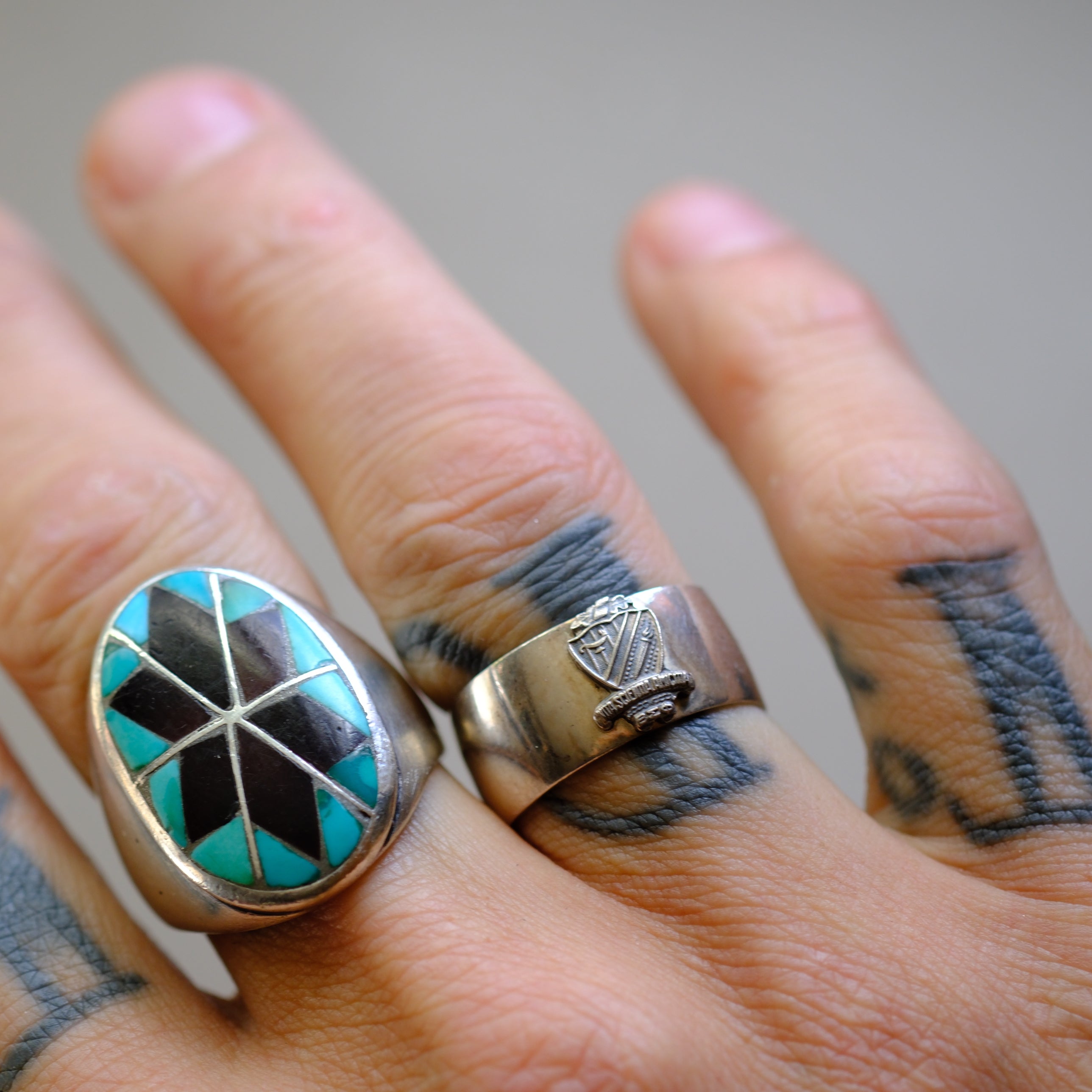 Close-up of a hand wearing two silver rings with turquoise and black stone inlays.