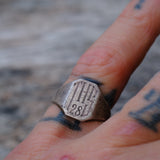 Silver ring with 'THE 281' engraved on a person's finger with tattoos.