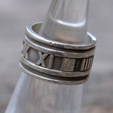 Silver ring with Roman numeral design on a blurred background